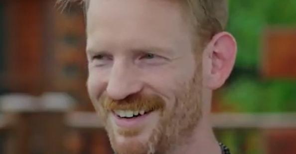 USMC Veteran Paul Downs smiles with cabins and greenery in the background