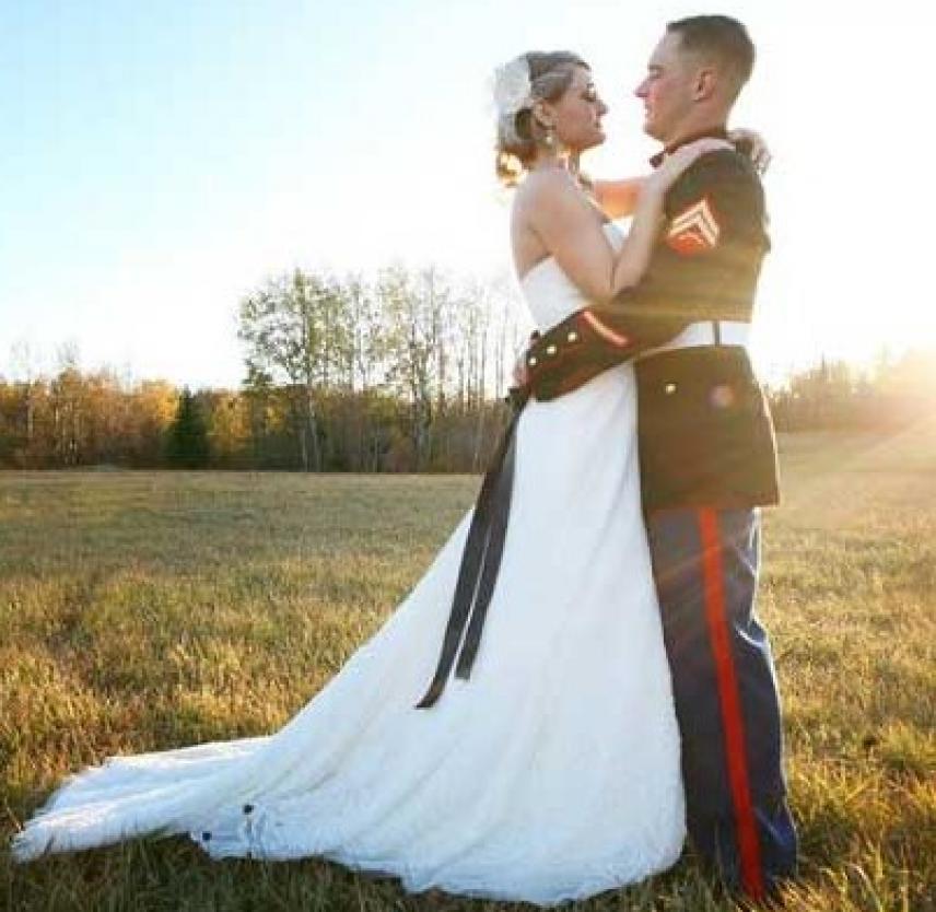 Brett and Whitney Foley on their wedding day. A Marine in full dress uniform hugs a blonde woman in a wedding dress with the setting sun behind them