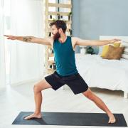 Man doing yoga warrior pose in a sunlit room.